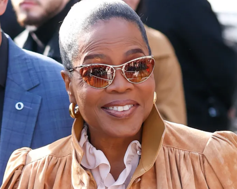 Oprah Winfrey at Paris Fashion Week Chloe Show wearing GIMME Tigga Tube Hoops, sunglasses and a peach, suede jacket.