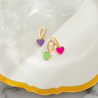 Purple, pink and green enamel heart shaped pendants with clear stone embellishments laying on a plate