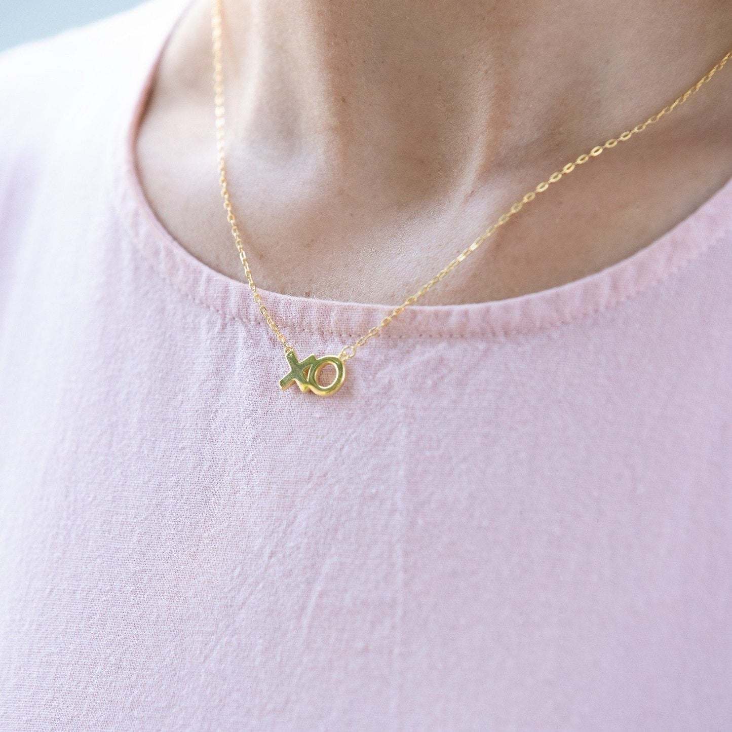 Woman wears a sterling silver necklace with 14k gold plating, that features 'XO' in text .