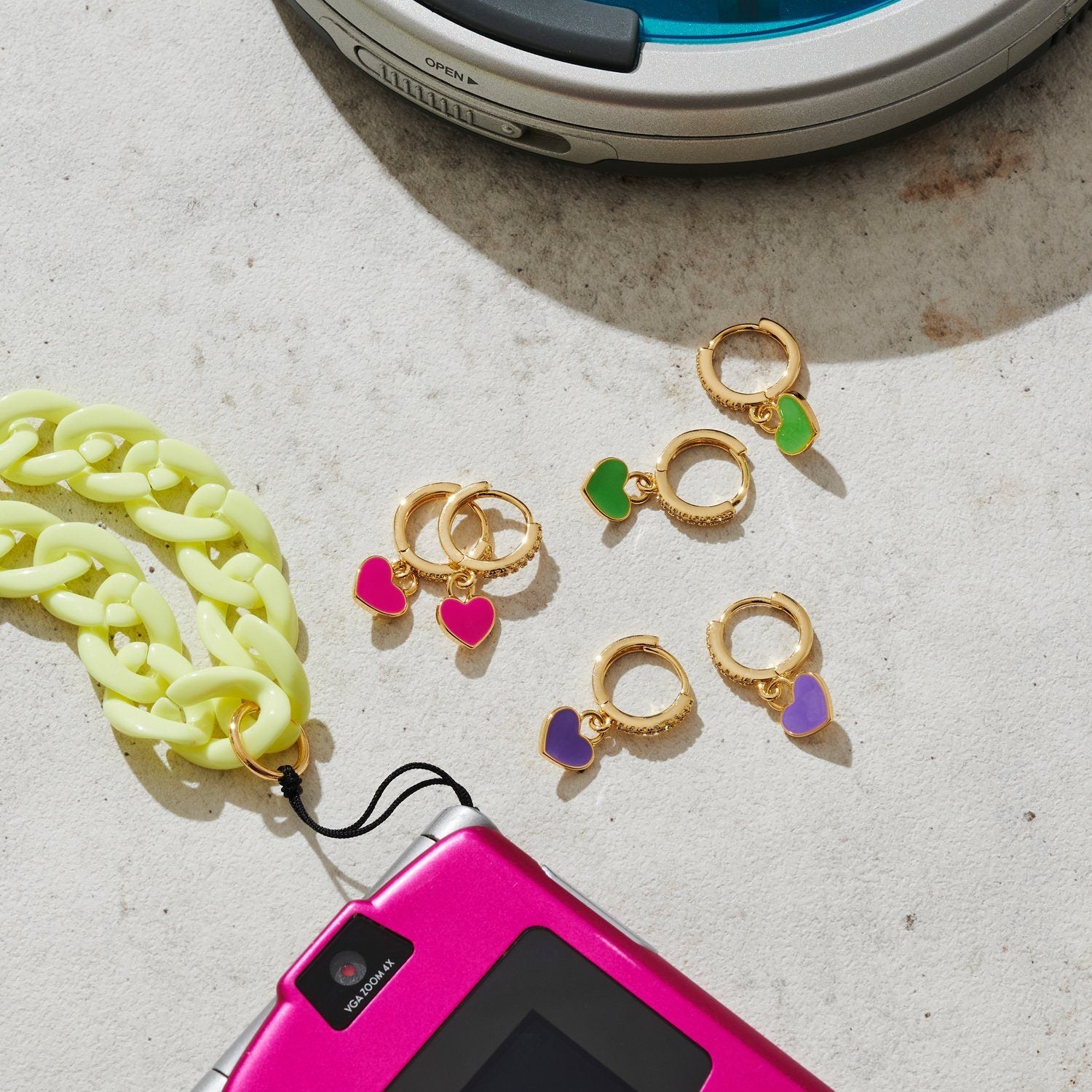 Flat lay of three pairs of small gold hoops with green, pink and purple pendants