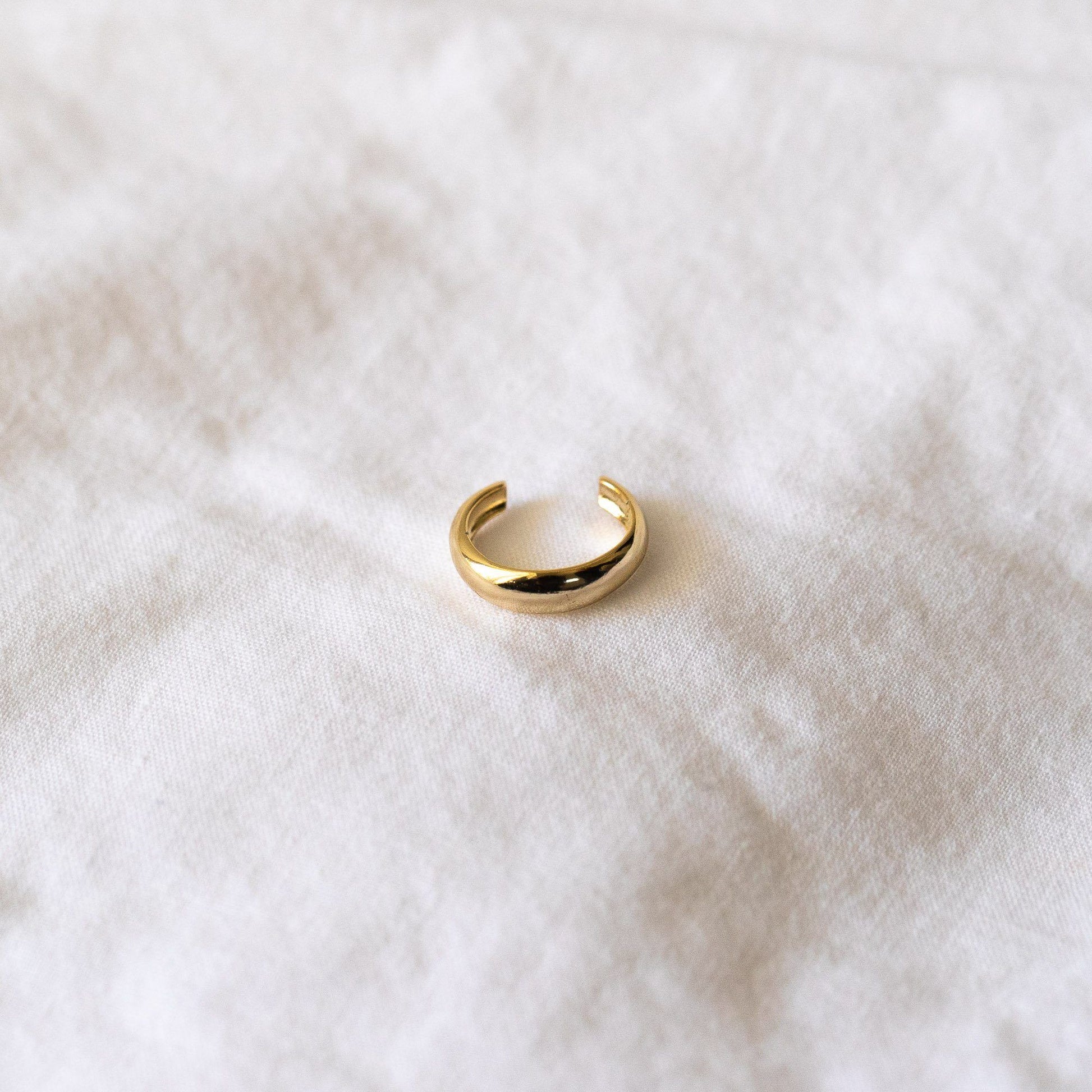 Flatlay of 3mm gold plated, sterling silver ear cuff to wear on conch. Sitting on top of plain, white sheet.